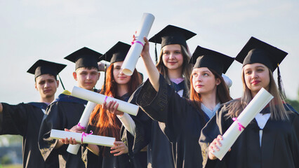Wall Mural - Cheerful graduates pose with raised diplomas on a sunny day.
