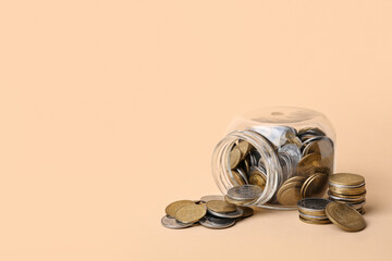 Overturned jar with coins on beige background. Savings concept