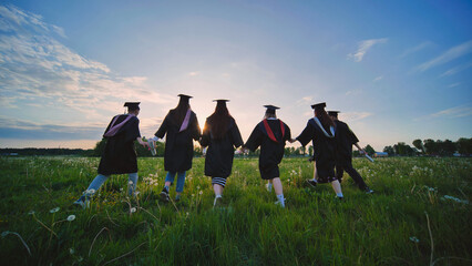 Wall Mural - Six graduates in robes walk against the backdrop of the sunset.