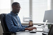 © Seventyfour - Side view of Black man in glasses typing on laptop and holding takeaway coffee cup while sitting at office desk in IT company