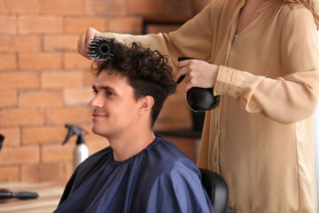 Poster - Professional hairdresser applying hair spray on young man's curly hair in beauty salon