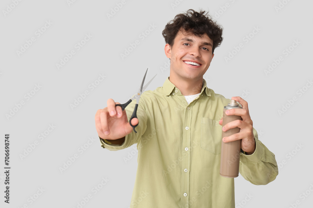 Handsome young man with hair spray and scissors on grey background