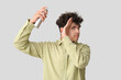 © Pixel-Shot - Handsome young man applying hair spray on his curly hair against grey background