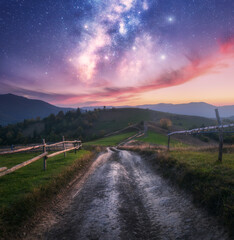 Wall Mural - milky way over the rural road, wooden fence, green hills in mountain valley at summer night. space. 