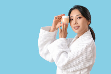 Poster - Beautiful young Asian woman with facial cream on blue background