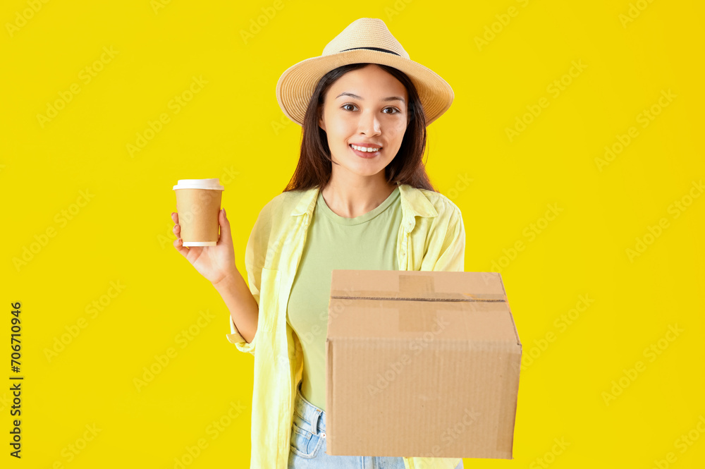 Young Asian woman with parcel and coffee cup on yellow background