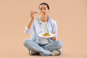 Wall Mural - Young woman eating tasty pasta on beige background