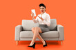 © Pixel-Shot - Young pin-up businesswoman with tablet computer sitting on sofa against orange background