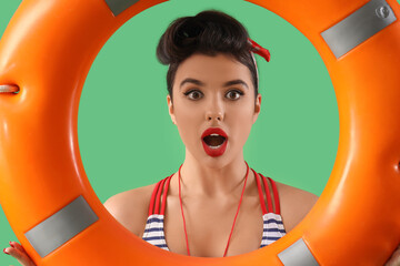 Shocked young pin-up lifeguard with ring buoy on green background, closeup