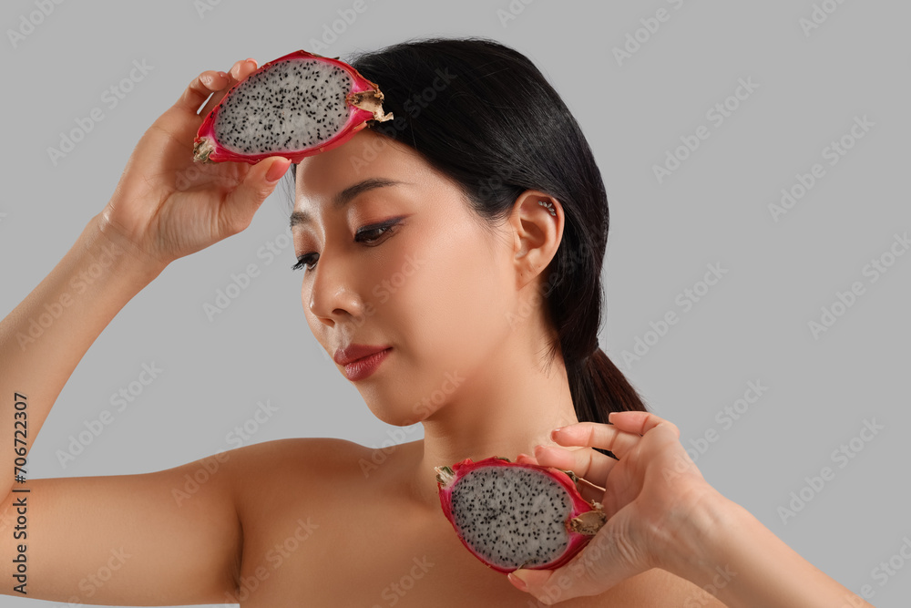 Pretty young Asian woman with dragon fruit on grey background