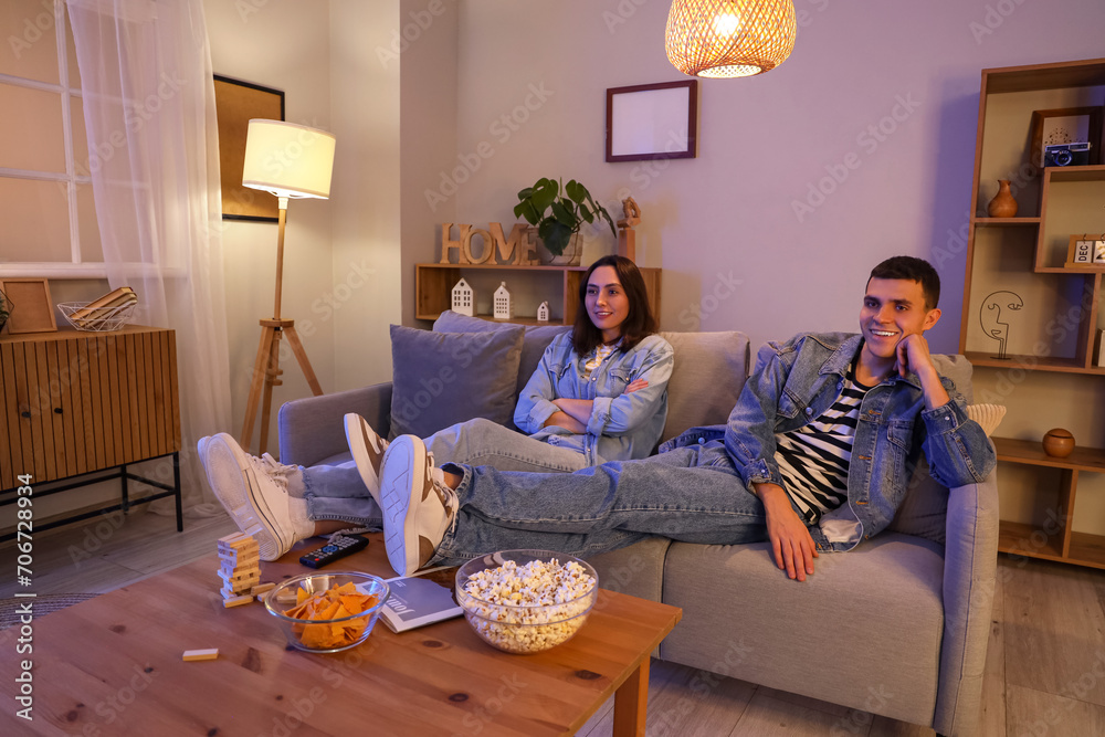 Young couple watching TV on sofa at home in evening