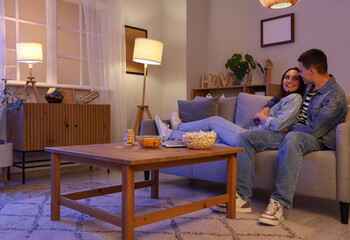 Poster - Young couple watching TV on sofa at home in evening