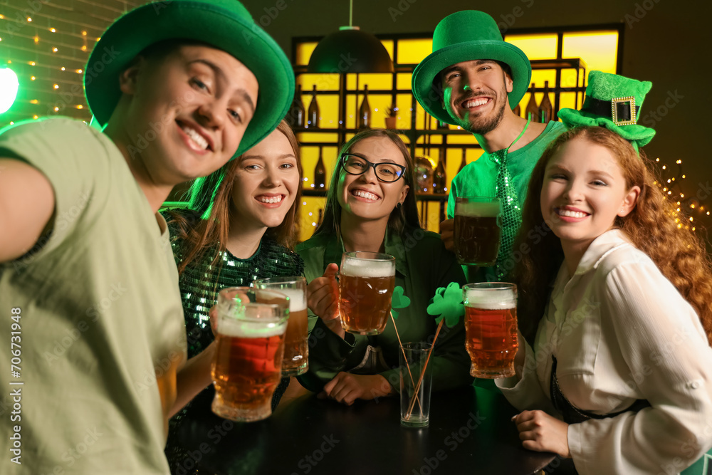 Group of young friends with beer celebrating St. Patrick's Day in pub at night