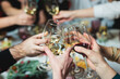 Group of guests celebrate and raise glasses, toasting and cheering with alcohol glasses with wine and champagne in the restaurant on corporate christmas birthday party event or wedding celebration
