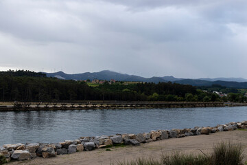 Wall Mural - a tranquil lake scene with a stone embankment, lush greenery, distant hills, and overcast skies. It exudes a peaceful, serene mood