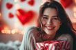 Happy young woman with gift box celebrating Valentine`s Day, adult girl on red heart shapes and lights background, romantic design. Concept of love, smiling people and romance
