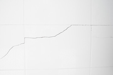 A white tiled wall with water droplets in the bathroom. Broken, cracked tiles. destroyed wall as a result of the earthquake.