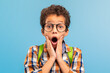 Shocked boy with glasses, hands on cheeks, blue background