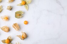 Ripe Physalis Fruits With Calyxes On White Marble Table, Flat Lay. Space For Text
