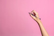 © Queenmoonlite Studio - Hand of young woman holding pen on pink background, closeup