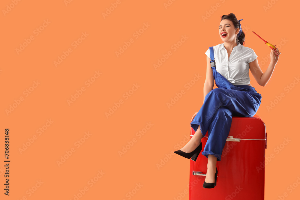 Attractive pin-up worker with screwdriver sitting on retro fridge against orange background