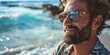 A man with a beard is pictured wearing sunglasses on the beach. This image can be used for various purposes, such as travel blogs, summer promotions, or lifestyle articles