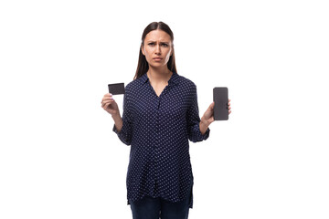 Wall Mural - young european slim brunette woman in blue clothes shows a credit card and a smartphone with a mockup