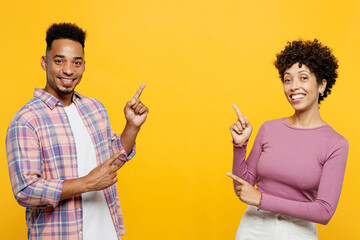 Wall Mural - Young smiling couple two friends family man woman of African American ethnicity wear purple casual clothes together point index finger on area between them isolated on plain yellow orange background.