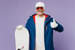 Happy smiling fun cool man he wear warm blue windbreaker jacket ski goggles mask hat hold snowboard show thumb up spend extreme weekend winter season in mountains isolated on plain purple background.