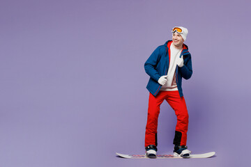 Wall Mural - Full body smiling fun man wear blue windbreaker jacket ski goggles mask hat snowboarding look aside show thumb up spend extreme weekend winter season in mountains isolated on plain purple background