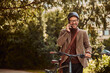 A smiling businessman pushing a bicycle to home from work while talking on a mobile phone.