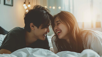 Wall Mural - Lovely cute smiling young Asian lover couple lying on elbow on the bed and laughing while talking funny in the bedroom at home. Concept of romantic relationship.