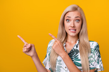 Wall Mural - Photo of funny impressed woman with straight hair dressed shirt directing empty space biting lips isolated on yellow color background