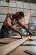 © Prins Productions - African male lines up piece of wood while working on carpentry project in woodwork warehouse