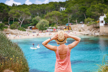 Wall Mural - Rear view of a young woman in straw hat looking at Cala Gat beach in Mallorca