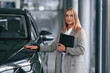 © standret - With tablet in hands. Woman in formal clothes is in the car dealership