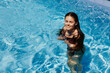 Happy woman swimming in the pool in red swimsuit with loose long hair in the sunshine, skin protection with sunscreen, concept of relaxing on vacation.