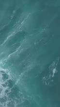 Vertical Aerial Top View Of Turquoise Sea Waves Foaming And Splashing, Big Waves From Above Rolling And Breaking On Empty Ocean Beach On Cloudy Day
