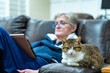 Cat sitting with a senior woman reading a tablet - focus on the cat