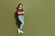 Full length photo of pretty optimistic girl wear oversize t-shirt denim pants hold hands crossed isolated on green color background