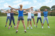 Jumping jacks, women and group outdoor for exercise on sports field and energy for cardio in fitness class. Health, wellness and training together, athlete team workout in park and physical activity