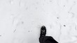 Point of view to male foot stepping on snowy path at winter park. Legs of young man in sneakers kicks up white snow going at forest. Guy walking at nature. Slow motion