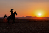 Fototapeta  - silhouette cowgirl in the sunset riding in the prairie near a waterhole