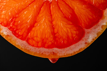 Wall Mural - Slice of red grapefruit with juice drops on a black background, macro photography. Texture fresh citrus fruit, closeup