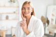 © Prostock-studio - Blonde lady enjoys her skincare routine touching cheek in bathroom