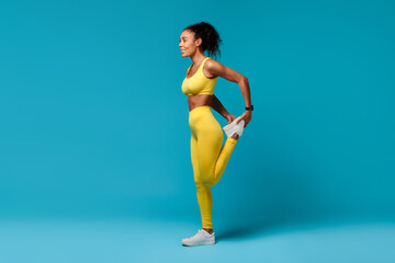 Wall Mural - Black woman warming up stretching leg muscles over blue background