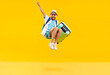 © Studio Romantic - Full body photo of a funny young happy man in sunglasses carrying his blue suitcase jumping and having fun on a yellow background. Summer holidays, vacation trip and travel concept.