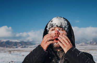 Wall Mural - Young man touching his face with snow on mountains background in winter