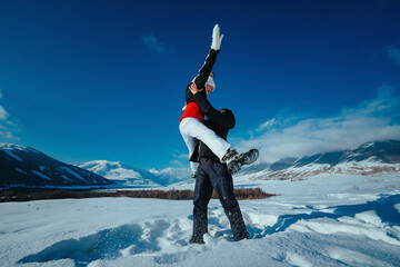 Wall Mural - Happy young couple of tourists having fun in the snowy mountains in winter, man tosses a woman in the air