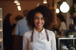 Cheerful woman with an apron looking directly at the camera with a charming smile welcoming guests in a successful restaurant